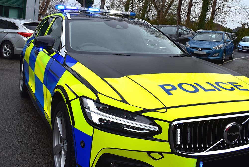 Close up of police car with various emergency lights on against other cars in a car park